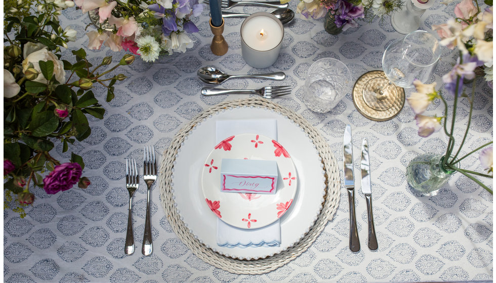 An aerial shot of a place setting, with a block printed tablecloth, silver cutlery and a printed dinner plate. 