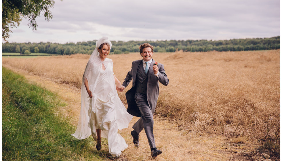 The bride and groom running together in a field. 
