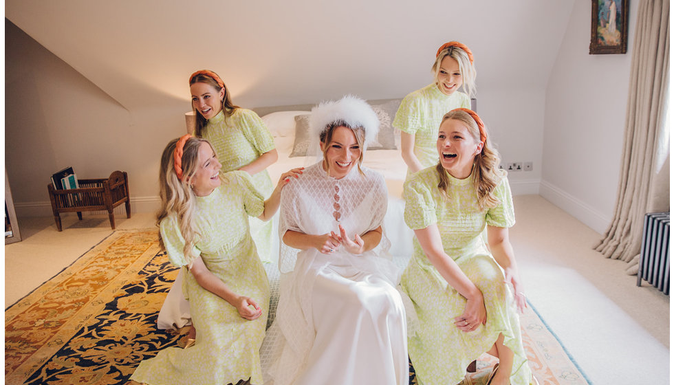 The bride and her bridesmaids sitting on a bed. The bridesmaids all wear yellow dresses with a red headband.