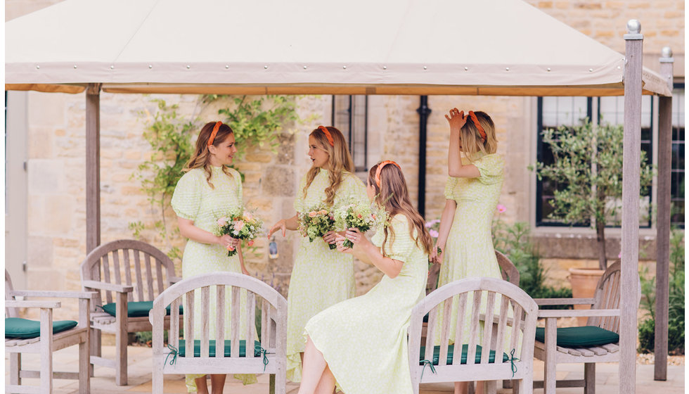 The bridesmaids all underneath a small marquee chatting holding their bouquets.