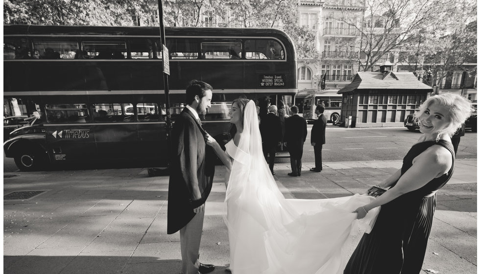 The bridesmaid holding the brides dress whilst she talks to Ed in front of a vintage London bus.