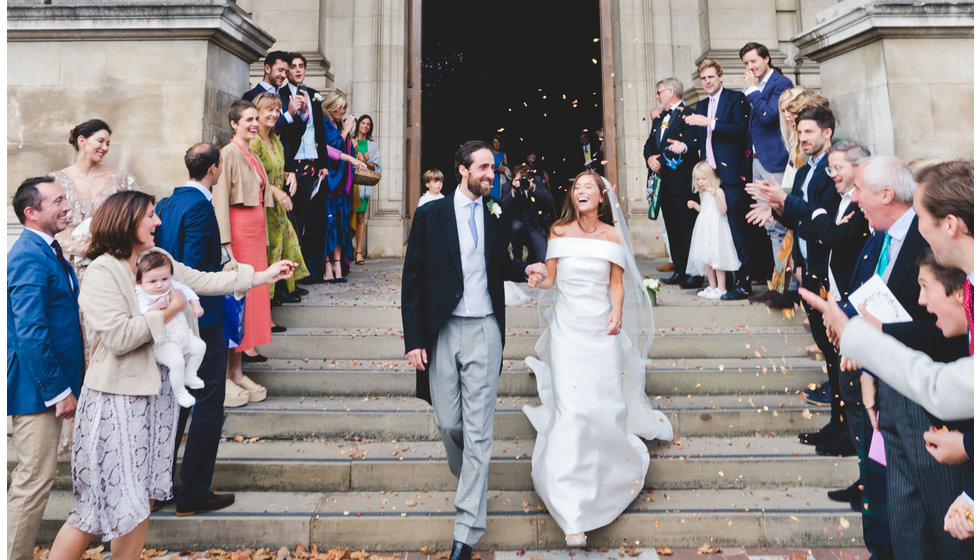 The bride and groom walk down the steps whilst their guests through confetti on them.