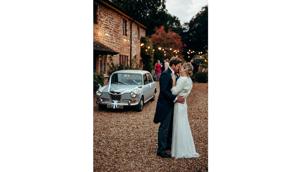 The bride and groom kissing in front of their vintage car and festoon lights.