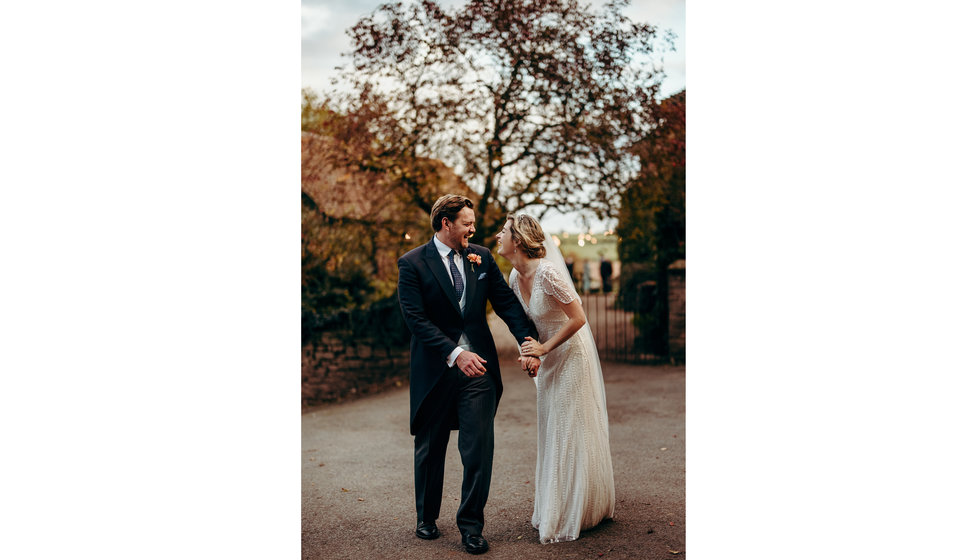 The bride and groom laughing and holding hands outside in the Autumnal Herefordshire countryside.