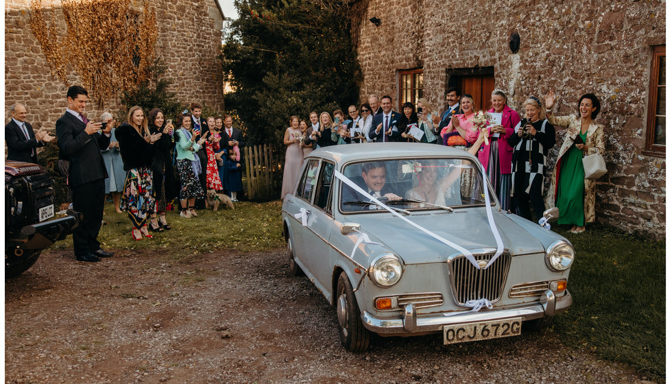 The bride and groom driving off in their decorated vintage car.