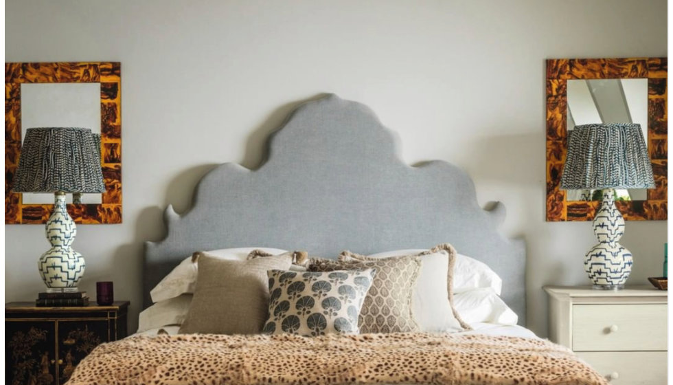 An oka bed with grey and white scatter cushions styled with a fur throw.