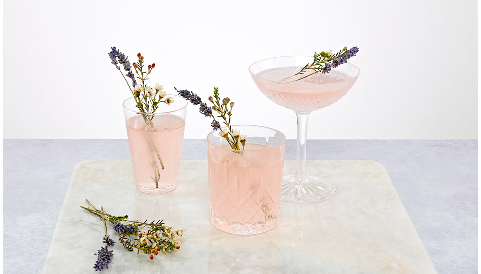 Sparkling pink cocktails in 3 different types of glassware, a couple, a classic cut glass tumbler and a dainty water glass with ferns on.