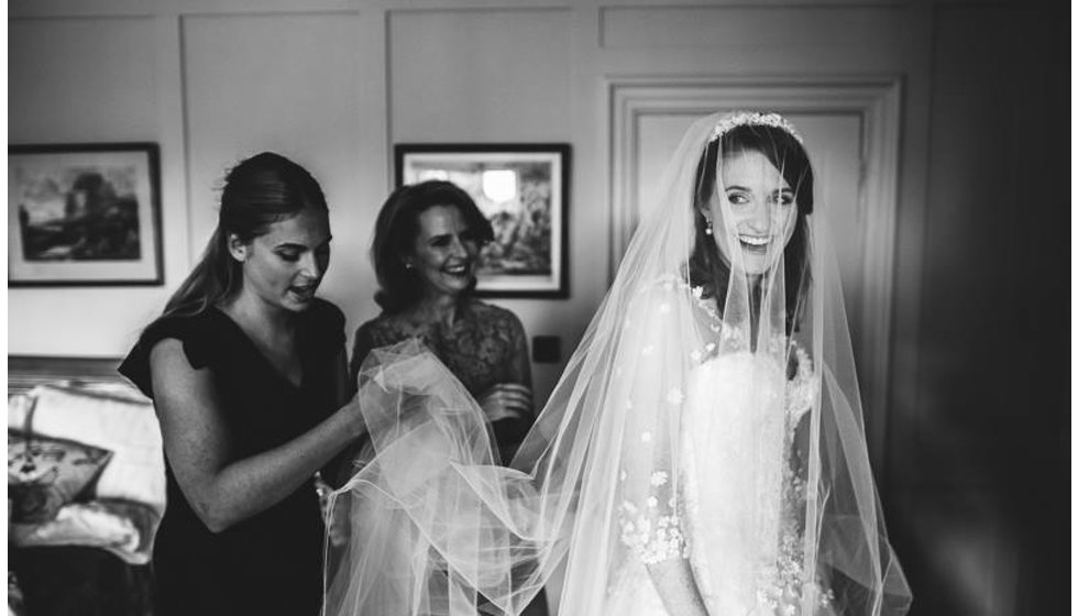 The bride in her Sassi Holford wedding dress and veil with her maid of honor and mother getting ready before her wedding.