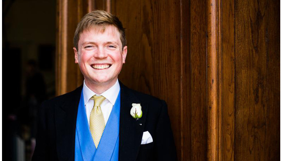 The groom standing outside the Church wearing a traditional morning suit, a blue waistcoat and a yellow tie from Hermes. 
