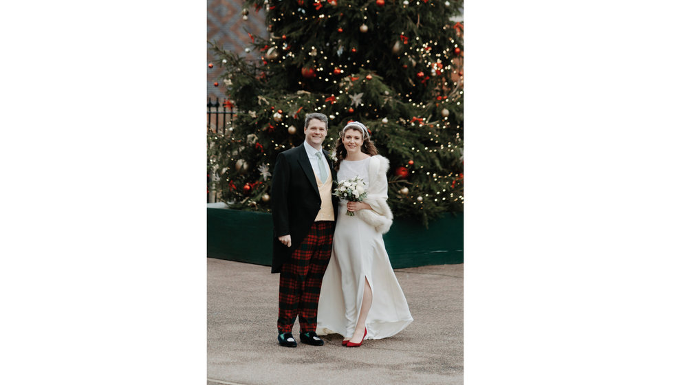 Sarah and Fergus by a large Christmas tree outdoors after their church wedding.