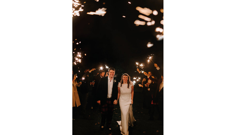 Sarah and Fergus on the evening of their small winter wedding outside their stretch tent - guests hold sparklers for their exit. 