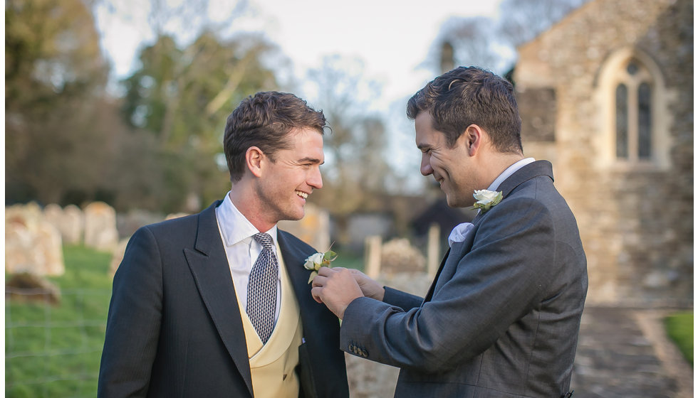 A groom being helped with his button hole by his brother outside the Church.