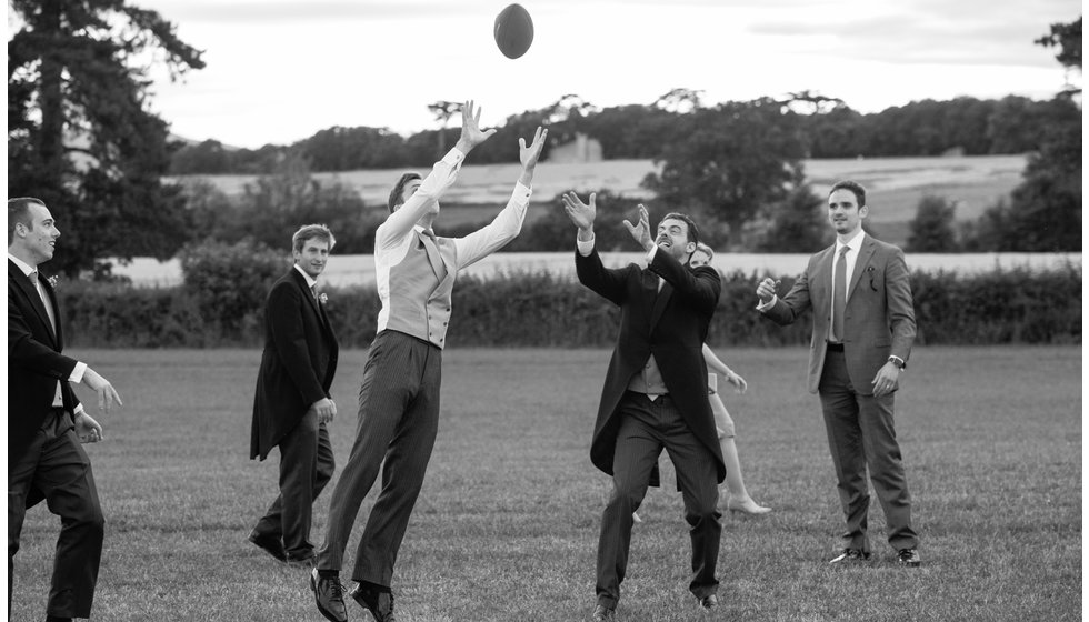 Men at a summer wedding playing rugby in their morning suits.