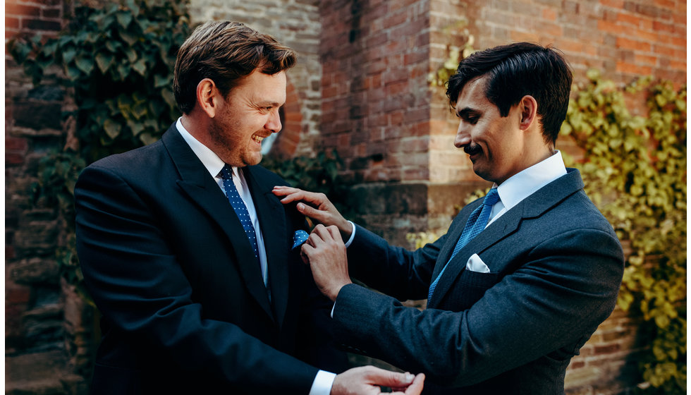 Groom being helped with his button hole by best man, both wear navy blue suits,