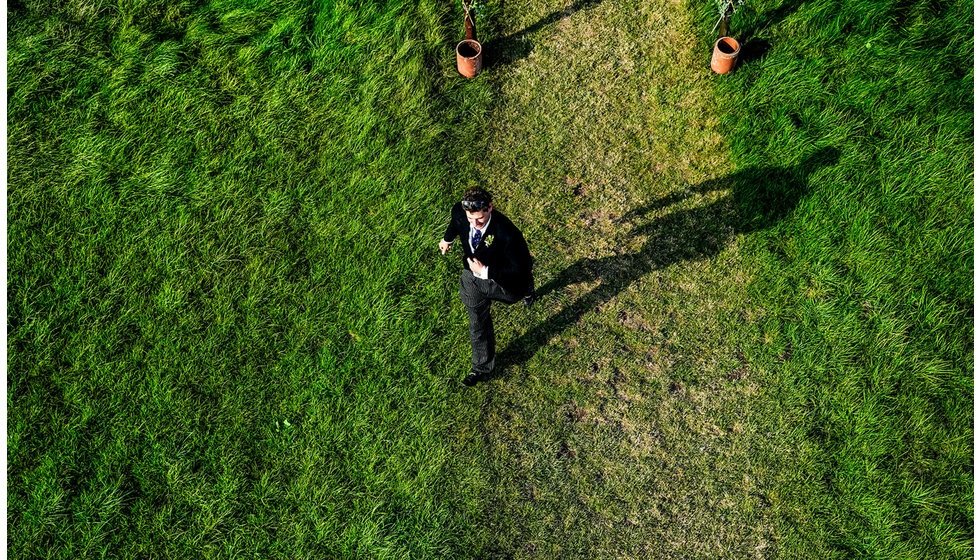 An overhead shot of a groom walking in the countryside in his morning suit on a summer day.