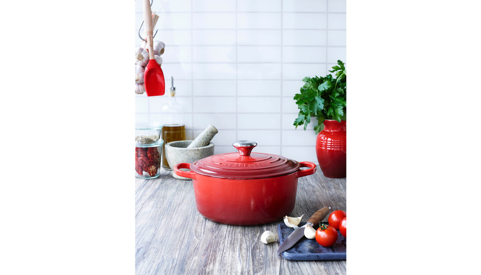 A classic red cast iron casserole dish from Le Creuset sitting on the side in the kitchen. 