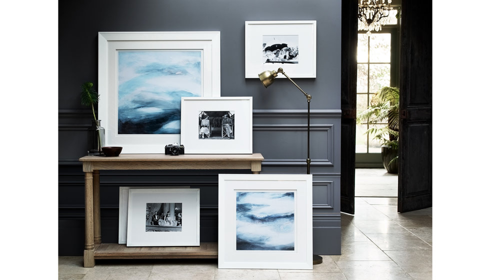 A selection of abstract landscapes framed in white frames styled in a hallway. 