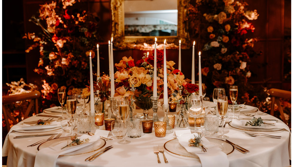 Sophie and Graeme's wedding breakfast table at Langrish House. The table is adorned with white taper candles, roses and white table linen. 