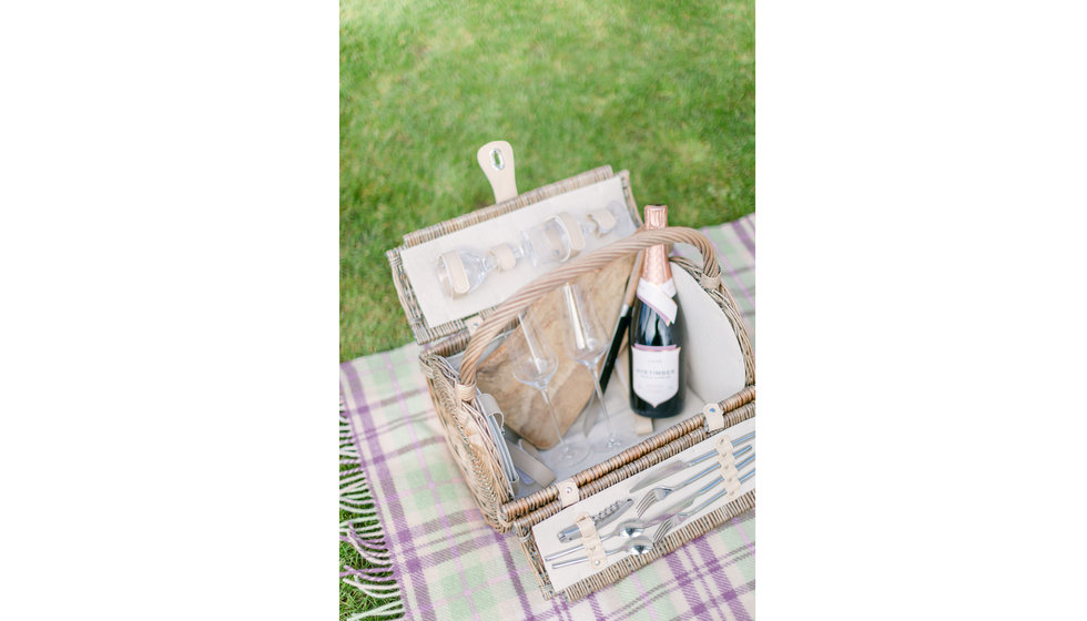 A Willow and Wicker Barrel Picnic Hamper laid on a Burgundy and Green stripe rug. 