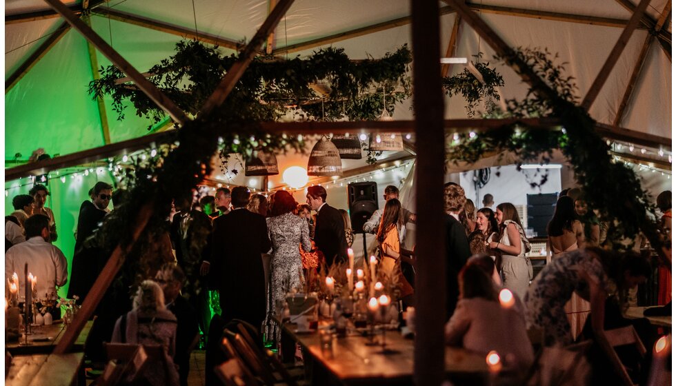 Chloe and Ed's wedding marquee, full of foliage, hanging wicker shades and candlelight