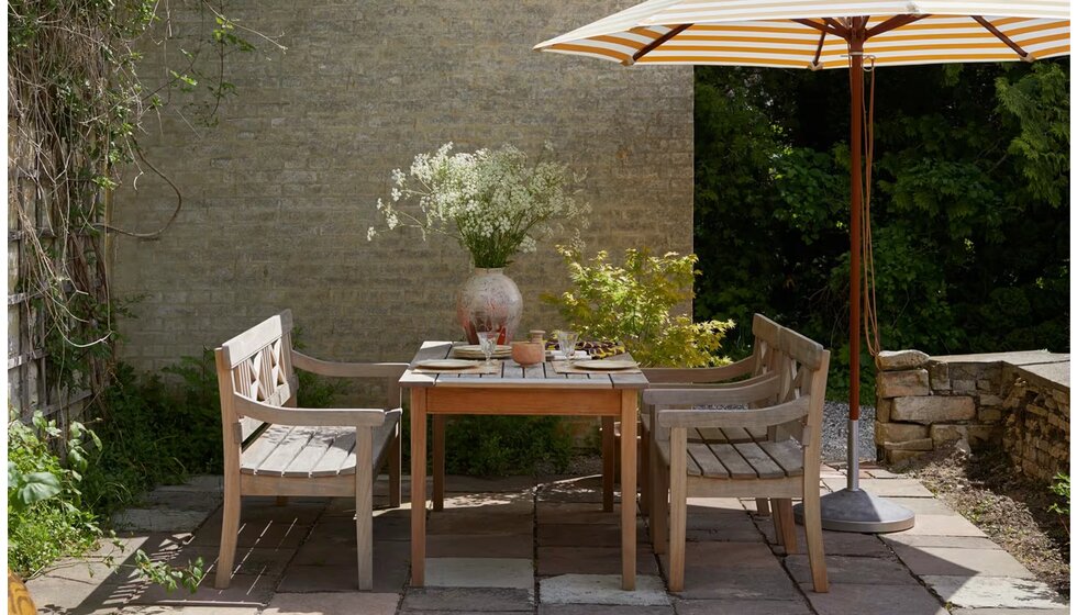 Special Wedding Gift List Ideas for the Garden | A Sun-lit Terrace with Wooden Garden Furniture, Flowers in a Vase, and a Yellow Striped Umbrella