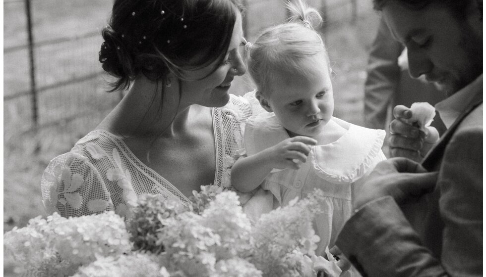 Whimsical Floral Wedding in London Park | Black and white photo detail of the bride in a floral dress holding her small daughter while she pins on a wedding corsage.