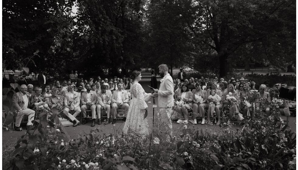 Whimsical Floral Wedding in London Park | A black and white photo of the wedding ceremony with the groom and bride saying their vows in front of seated wedding guests