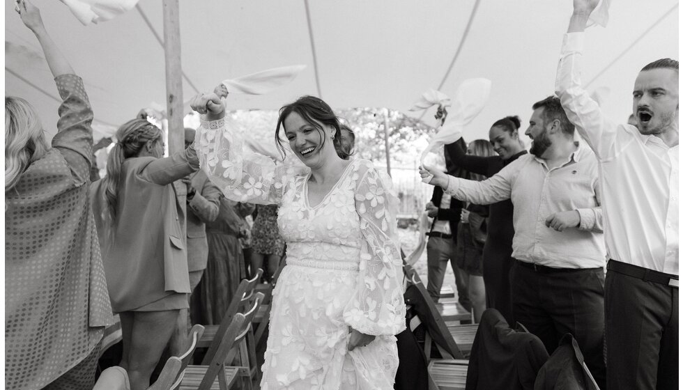 Whimsical Floral Wedding in London Park | A black and white photo detail of wedding guests waving napkins while the bride is entering the wedding reception tent