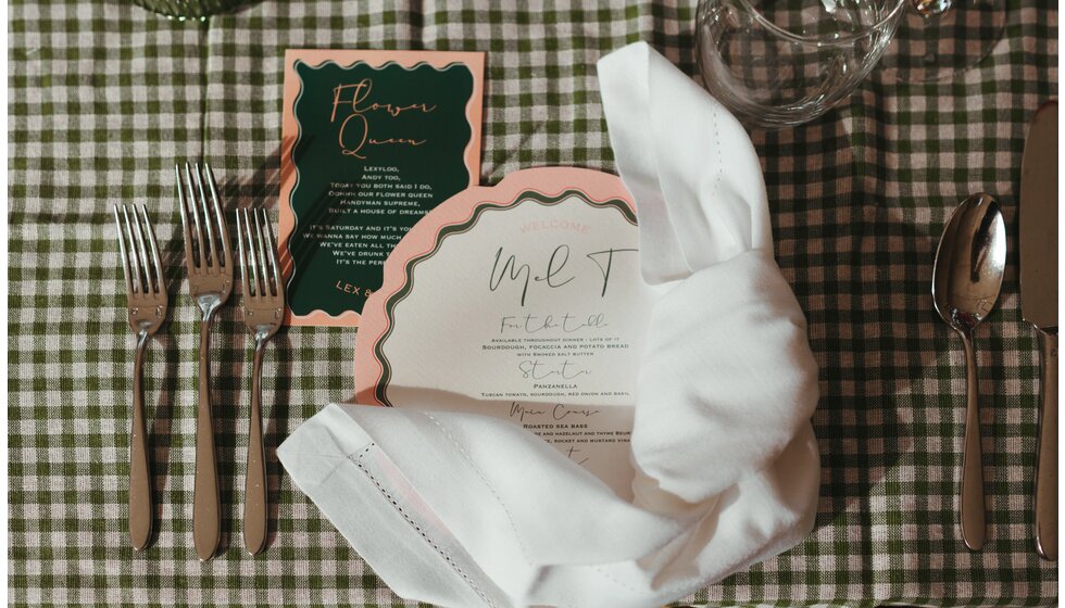 Whimsical Floral Wedding in London Park | Details of the blush and green wedding stationery placed with a white napkin on a plate and gingham tablecloth