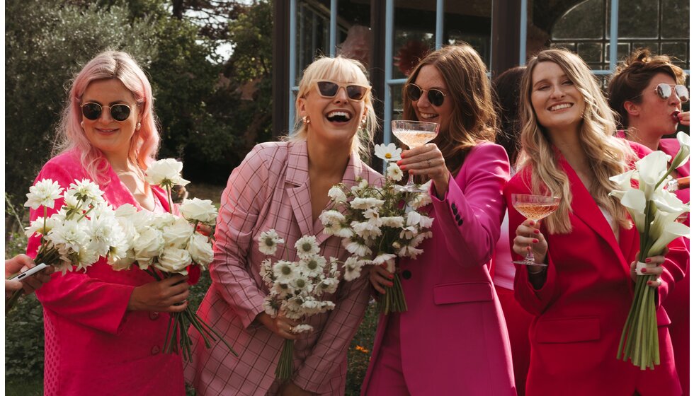 Whimsical Floral Wedding in London Park | Bridal party wearing pink bridesmaids suits and white flowers, while toasting with a glass of champagne