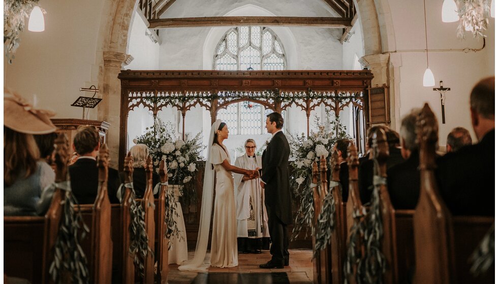 The Ultimate Wedding Planning Checklist | A traditional bride and groom are sharing their wedding vows in church in front of their wedding guests.
