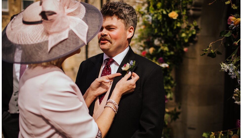 The Wedding Present Company | A mother of the groom puts a flower lapel on the groom before the traditional wedding ceremony.