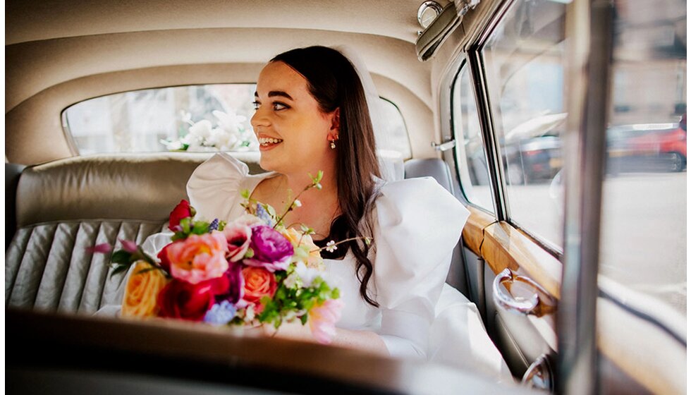 The Wedding Present Company | A bride with a colourful spring bouquet sits inside a vintage car before the wedding ceremony.