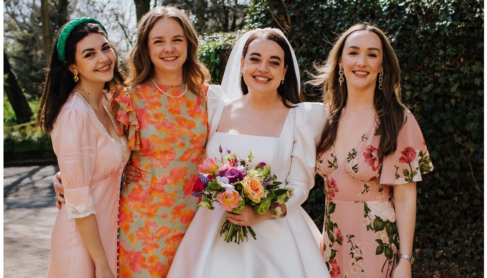 The Wedding Present Company | A bride in a Jesus Peiro traditional wedding gown stands next to her bridesmaids in pastel and floral dresses.