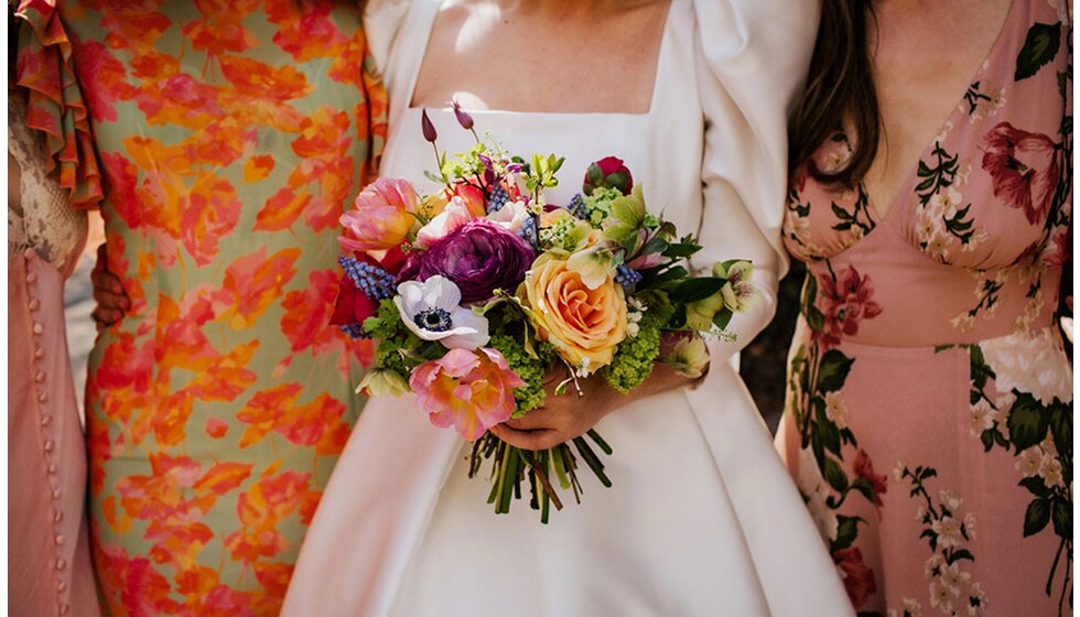The Wedding Present Company | A close-up of bridesmaids in pastel dresses and the bride in a Jesus Peiro wedding gown, holding a seasonal flower bouquet