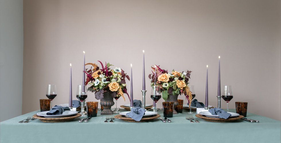 A tablescape laid with a green tablecloth, tall purple candles, autumnal flowers and wicker placemats.