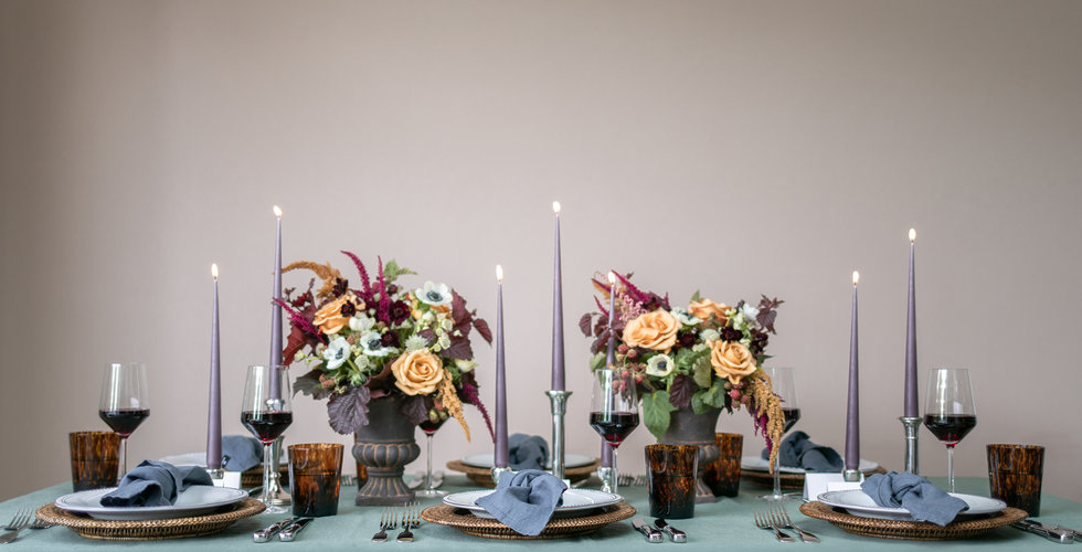 An autumnal tablescape with a green tablecloth, purple candlesticks and flowers in urns.