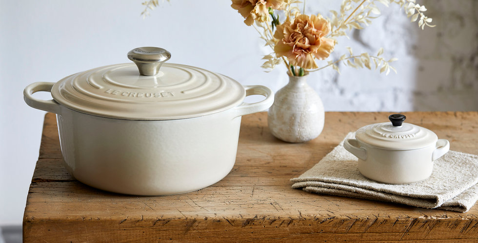 The round cast iron and a petite casserole in the meringue colourway on a wooden table.