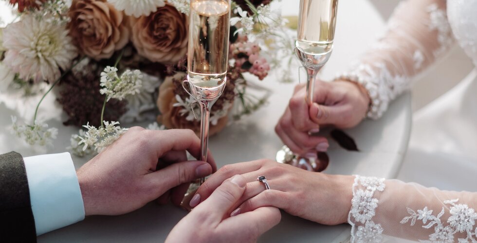 The Ultimate Wedding Planning Checklist | A close-up of a groom and bride's hands with an engagement ring on a flower-decorated wedding table